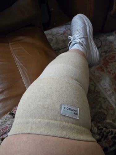 Close-up of a reviewer wearing the light-colored Premium Bamboo Knee Sleeve on their knee while resting.