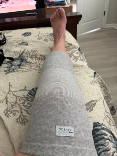 Customer resting their leg on a bed while wearing the gray Premium Bamboo Knee Sleeve.