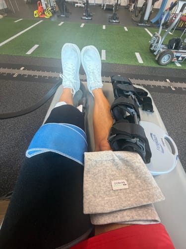 image 2 out of 2: Customer's gray Premium Bamboo Knee Sleeve folded next to their leg in a brace during physical therapy.