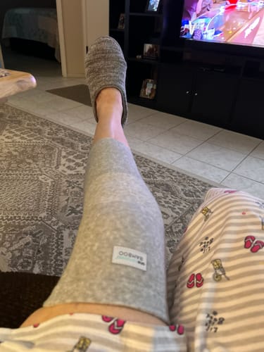 Customer's view of their leg propped up, showing the grey Premium Bamboo Knee Sleeve while relaxing at home.
