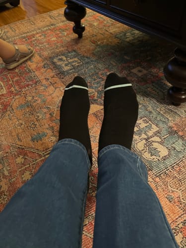 Customer's feet wearing black Premium Bamboo Compression Socks with blue jeans, resting on a patterned rug.