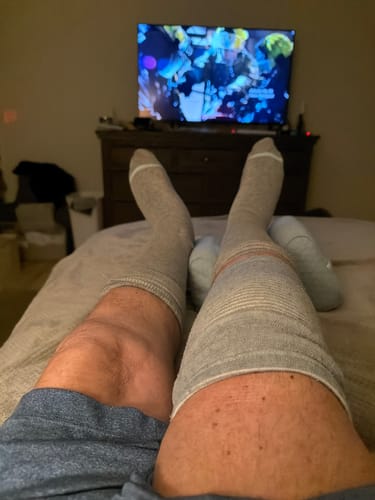 Reviewer relaxing in bed with their feet up, wearing grey Premium Bamboo Compression Socks.