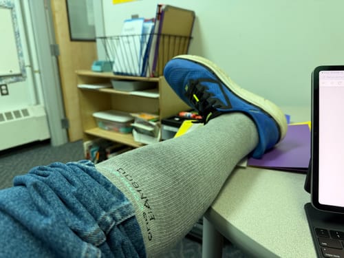 Customer wearing a grey Premium Bamboo Compression Sock and blue sneaker with their leg resting on a desk.