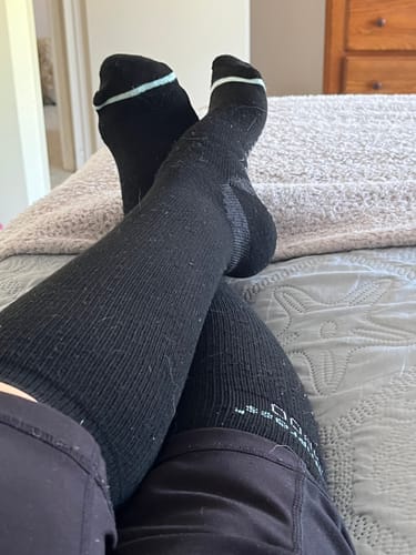 Customer relaxing on a bed with their feet up, wearing the black Premium Bamboo Compression Socks.