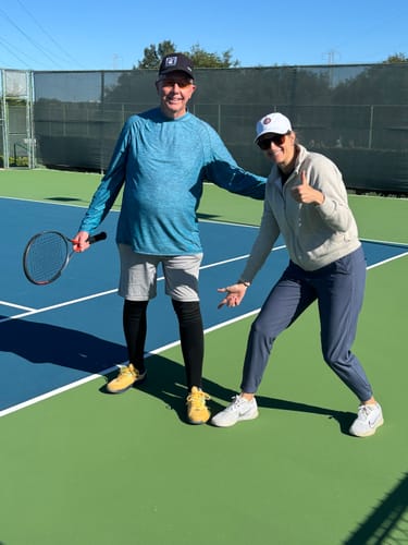 Customer wearing black compression socks while standing on a tennis court with a friend.